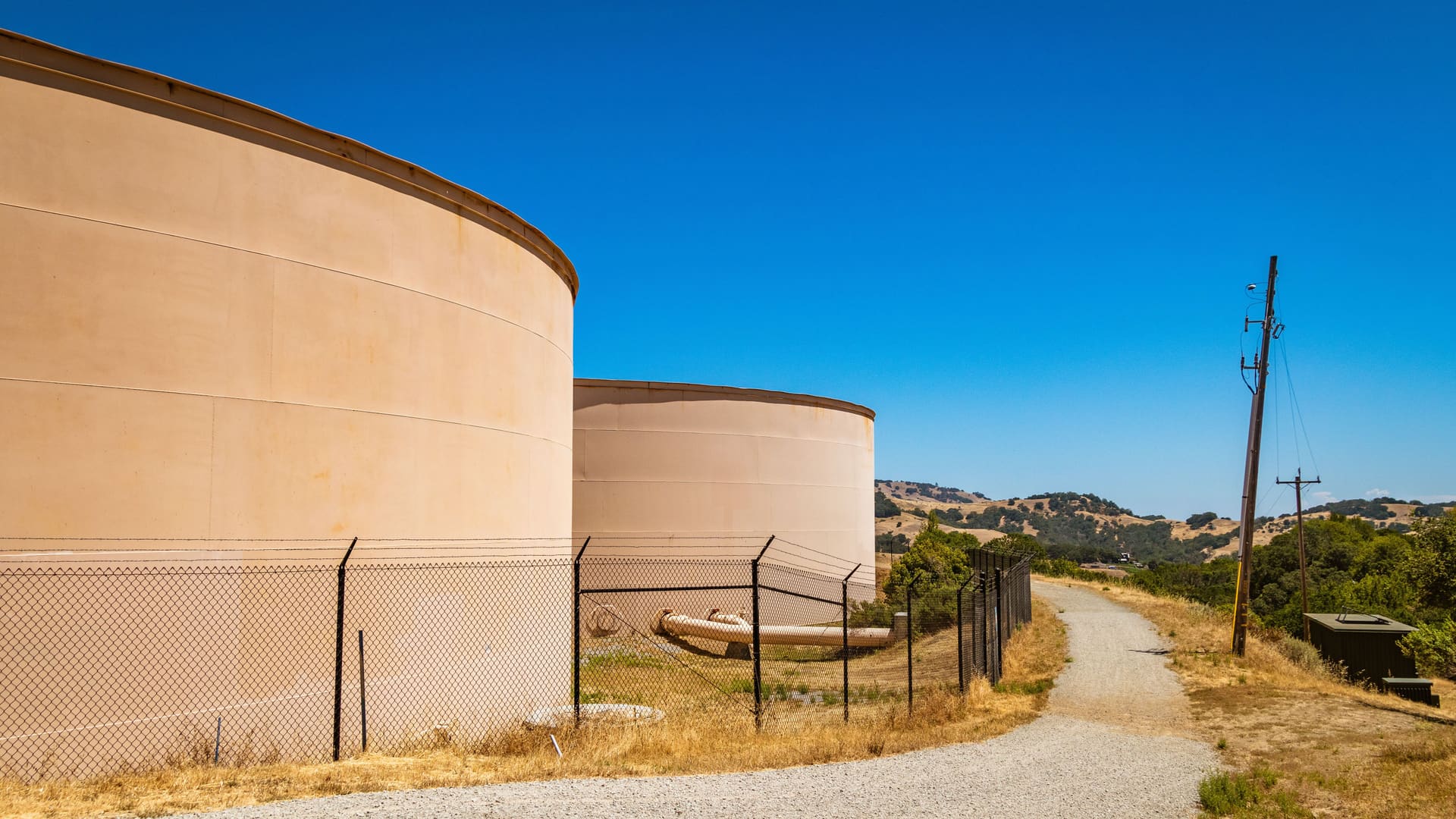 Welded steel ground-level water storage tanks behind a security fence on a dry hillside